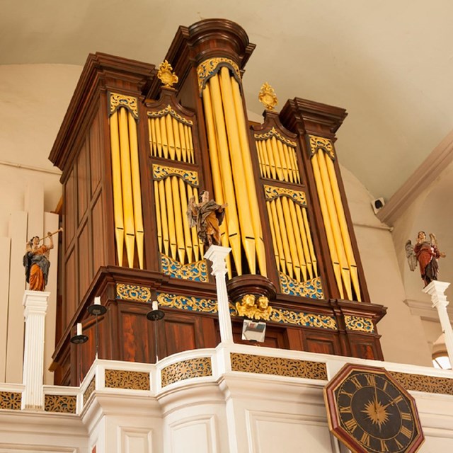 large organ with golden pipes on the second gallery floor of a church. Statues of angels flank it.