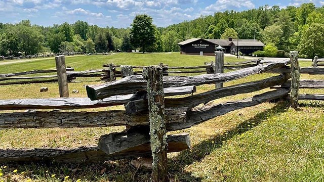A picture of a split rail fence with a brown on story visitor center in the background.
