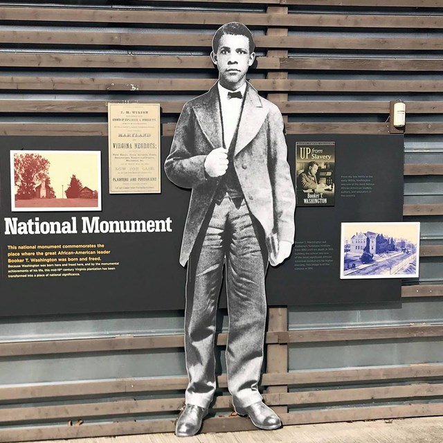 An image of a large format cutout of Booker T. Washington in a suit with posted information.