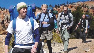 A group of four hikers with backpacks travel along a trail