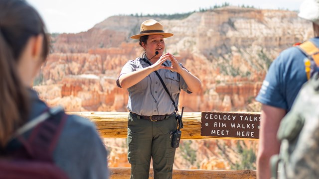 A park ranger in uniform stands in front of a group of people during a Geology Program 