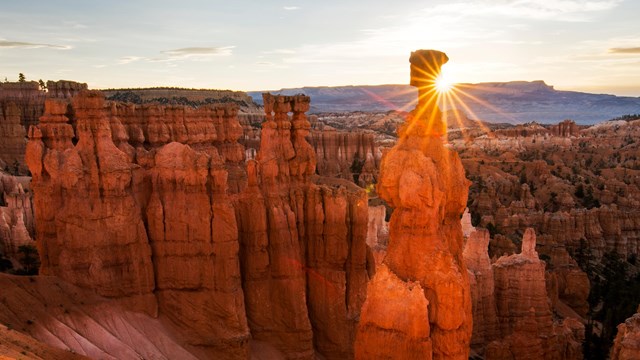 Red rock formations, including Thor's Hammer, against a sun flare