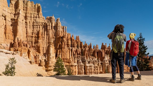Two hikers look out towards towering red rock formations