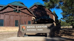 A metal sign reads Bryce Canyon National Park in front of a large brown building