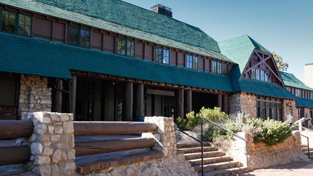 A large historic building built of brown logs with a green roof and stone patio