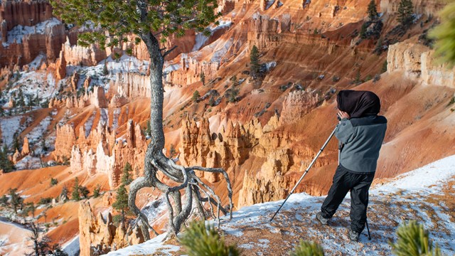 A man stands on the rim of the canyon with a large camera on a tripod.