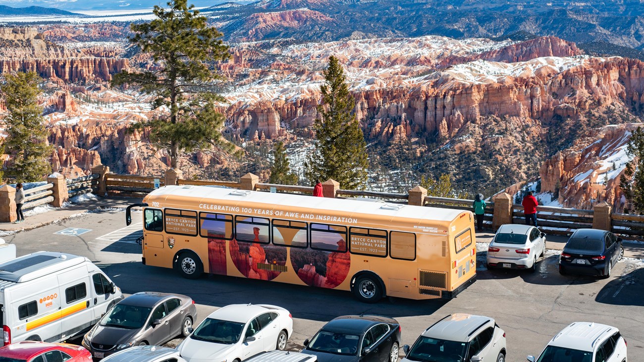 A large bus in a crowded parking lot against a background of red rocks