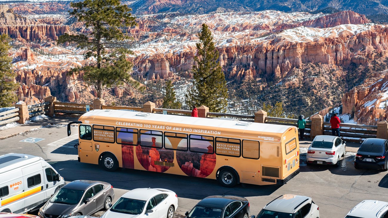 A bus stopped on the edge of a parking lot with rock formations in the background