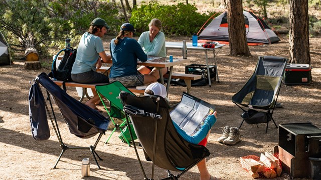 A group of people sit at a campsite surrounded by their gear.