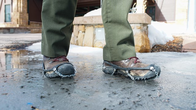 Boots with traction chains on them standing on ice patch