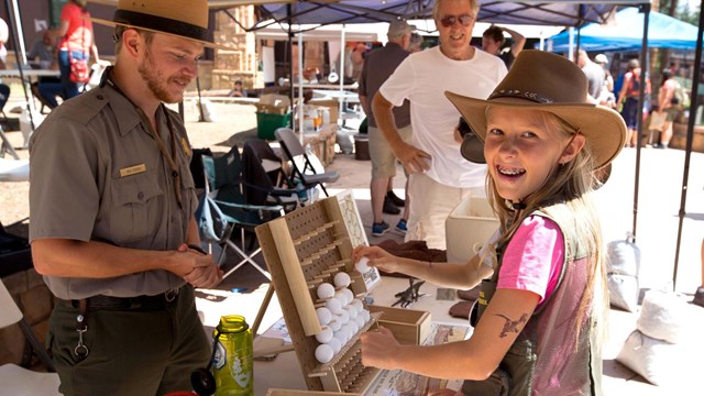 A girl smiles at the camera while playing a game while a ranger looks on.