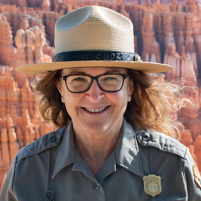 Woman in ranger uniform smiles at edge of red rock landscape