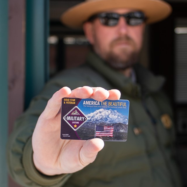 A man in a park ranger uniform holds a card that reads Military Lifetime pass.