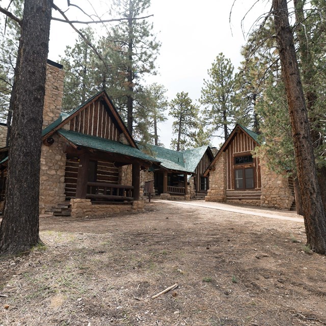 Two wood and stone buildings set between trees.