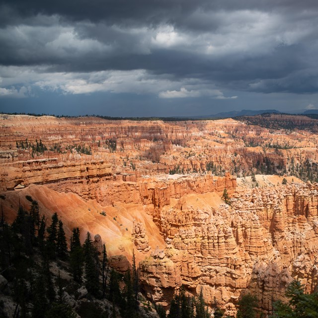 Dark clouds build above landscape of red rock spires, cliffs, and mesas.