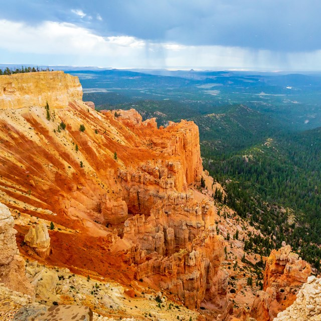 Red rock formations in the foreground with green forested areas in the background.