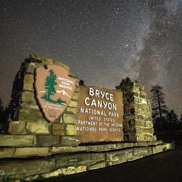 The entrance sign to Bryce Canyon with a dark sky and illuminated Milky Way behind it