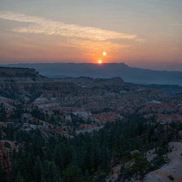 Photoshopped image shows two suns rising above a distant plateau above a forested landscape
