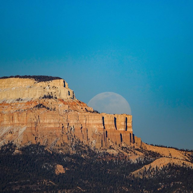 Full moon rises behind notched plateau