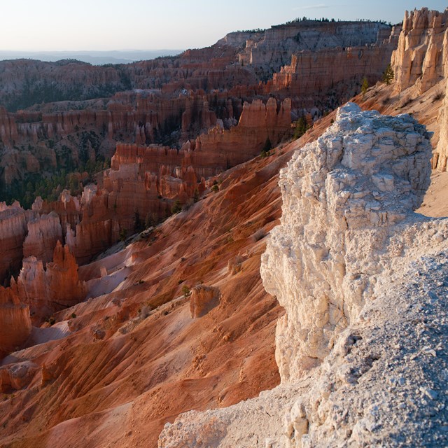 At the edge of a white cliff, a vast landscape of red rock spires, cliffs, and mesas.