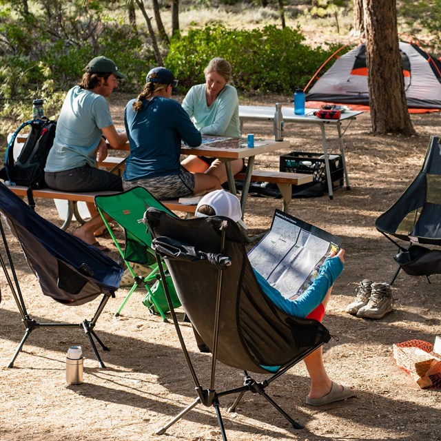 A group of people sit at a campsite surrounded by their gear.