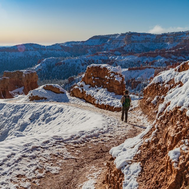 A single person hikes down a winding trail covered in snow and ice.