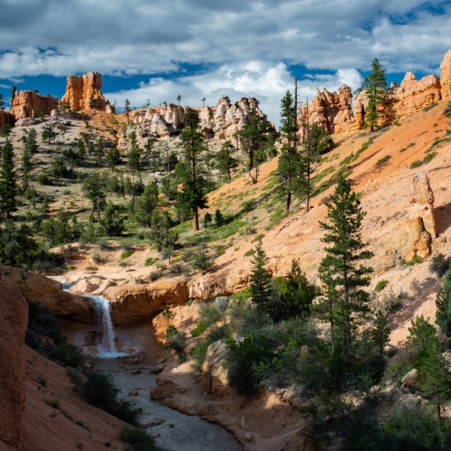 An overhead photo of a waterfall cascading into a creek surrounded by red rocks.