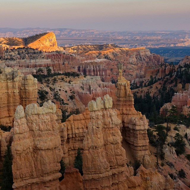 Red rock formations in the foreground and in the background other formations glow in the sun.