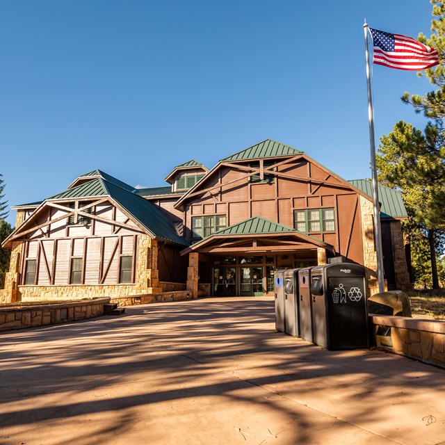 A wooden building with a dark green shingled roof and large windows with an American Flag out front.