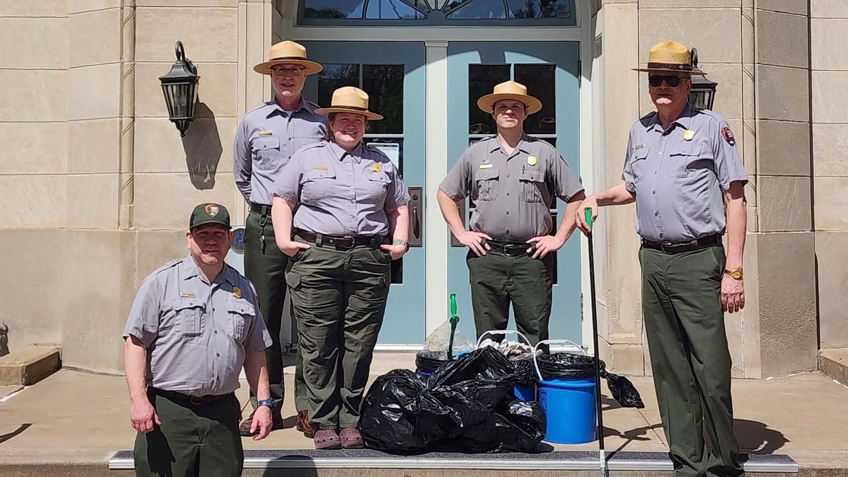 Park staff standing in front of Monroe Elementary School with bags of trash after trail cleanup.