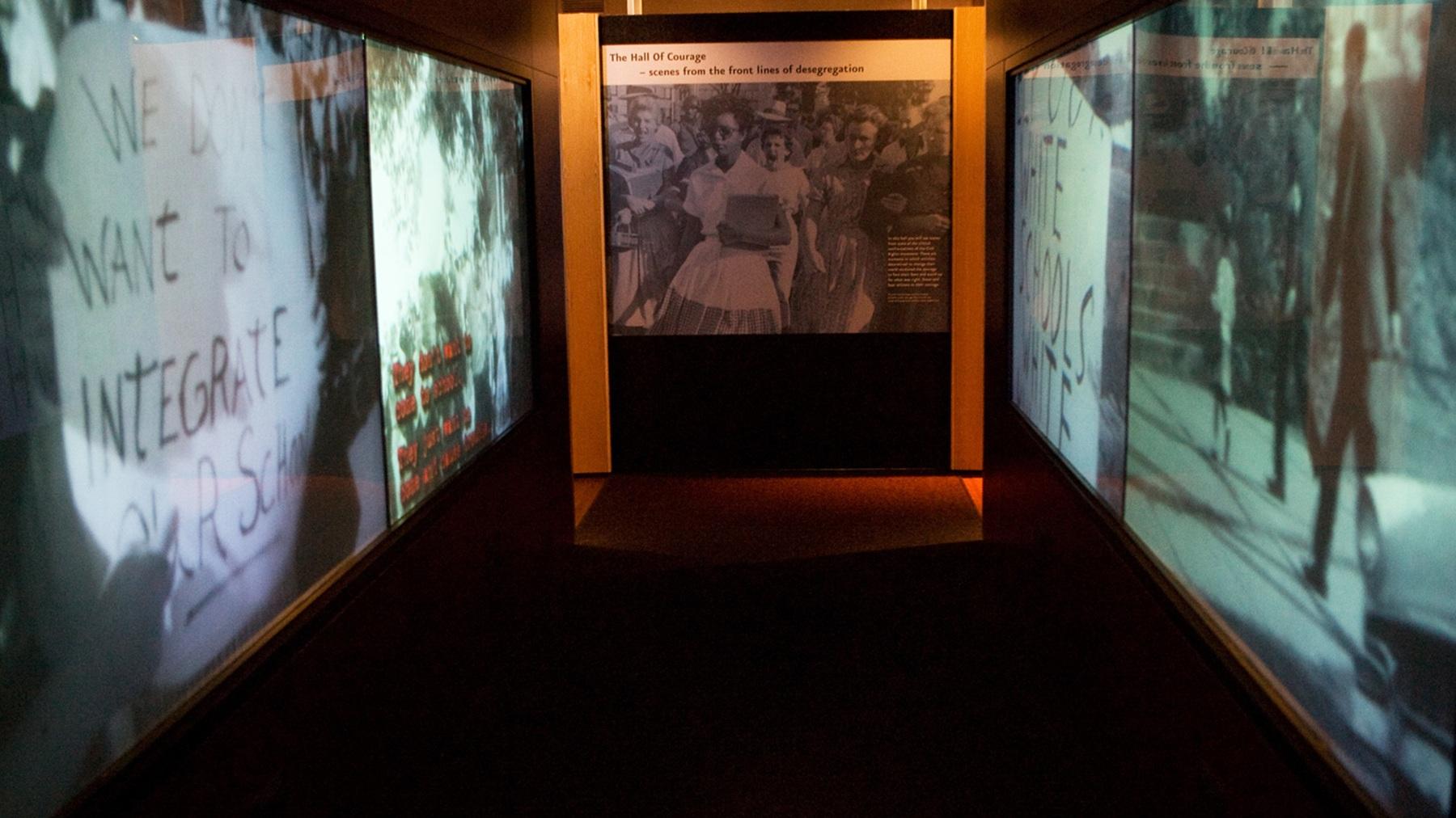 Image of a dark hallway with four projector screens to the left and right.