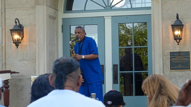 Joseph Walker plays saxophone to an audience in front of the former Monroe Elementary building.