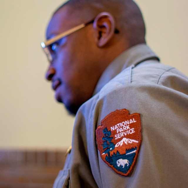 Side of park ranger with focus on the arrowhead  on their sleeve which reads National Park Service