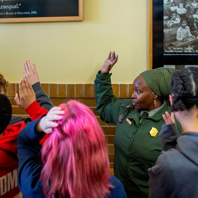 A park ranger raises her hand along with a group of children in front of a photo of discrimination.