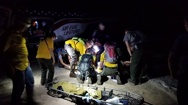 A group of first responders and park rangers loads a patient into a helicopter at night.