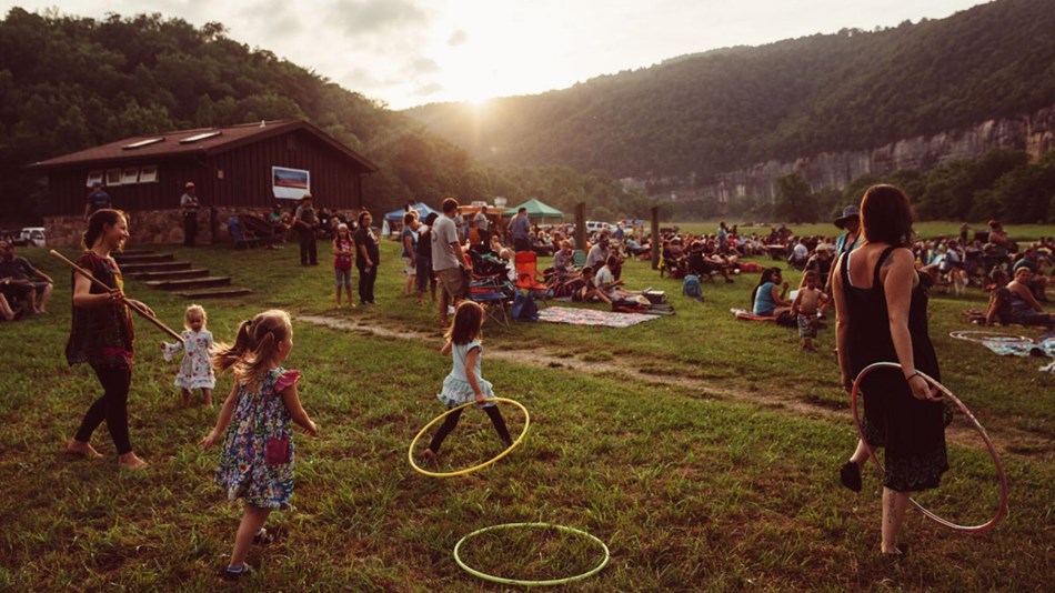 People with hula hoops and lawn chairs scattered along a grassy hill as the sun sets
