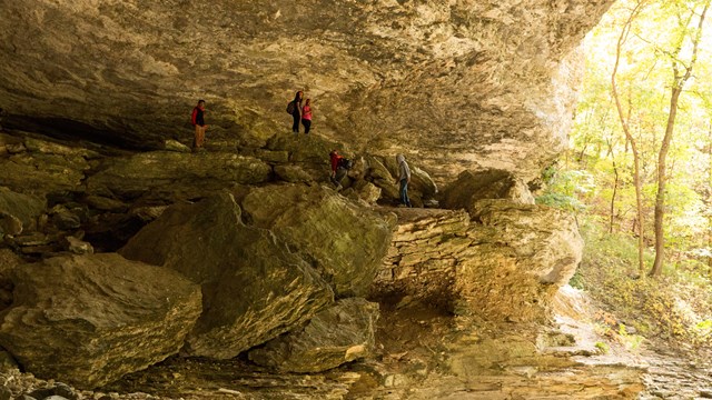 Hikers perch on top of large boulders beneath a bluff shelter