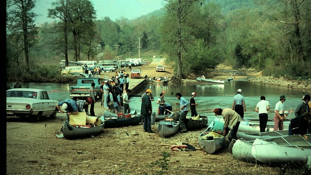 Canoeists prepare to launch as cars from the 1970s drive across the Ponca Low-Water Bridge