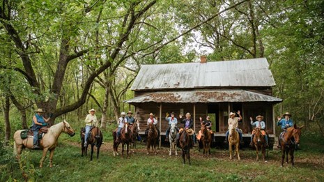 A group of horseback riders waves at us from the front yard of Granny Henderson's cabin