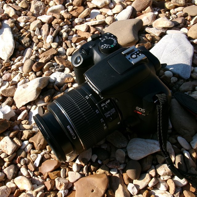 A digital camera sits on a rocky, gravel bar.