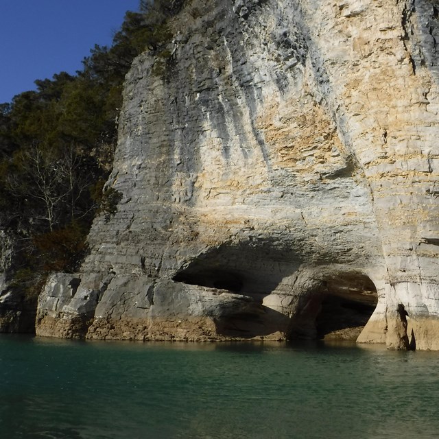 A limestone bluff with hollow openings along the bottom where it meets the river