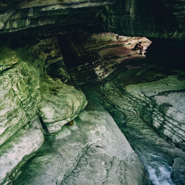 A long tunnel carved into rock with the silhouette of a hiker at the opposite end
