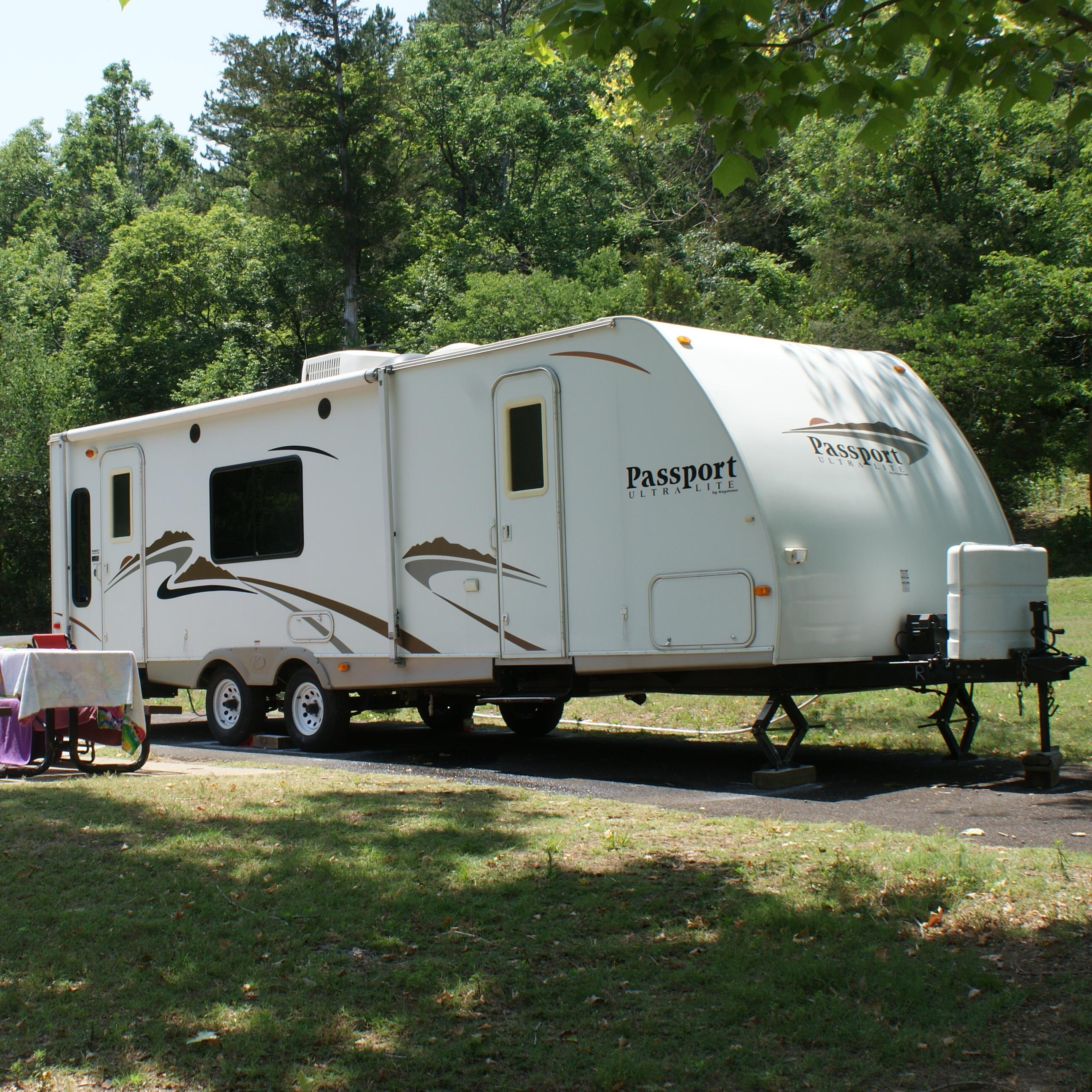 A large white camper trailer backed into a campsite. Beside the trailer is a picnic table. 