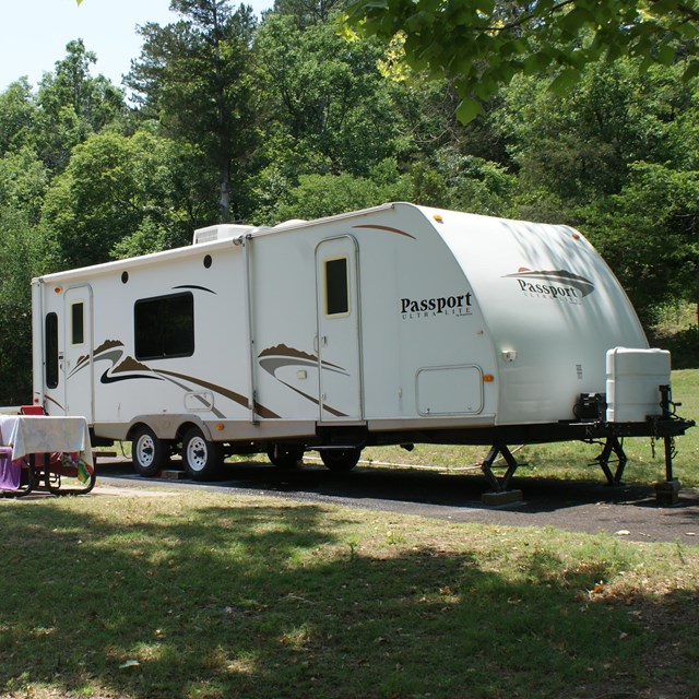 A large white camper trailer backed into a campsite. Beside the trailer is a picnic table. 