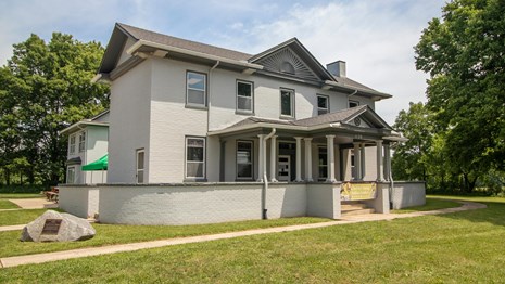 A large gray house with several windows under a blue sky with a green banner on the front porch