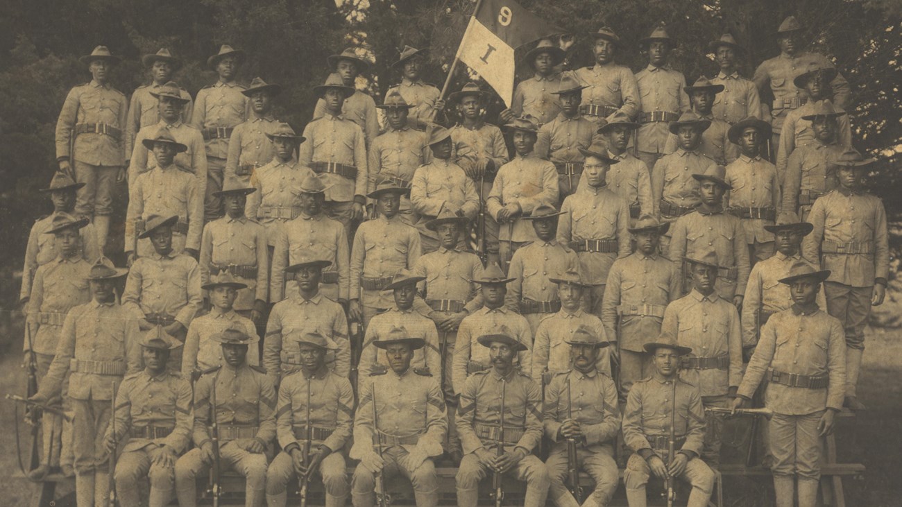 Several african american soldiers in uniforms on risers posing for a photo