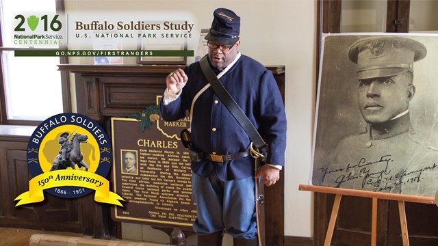 An African American ranger dressed as a Buffalo Soldier talks in front of a portrait of Chas. Young