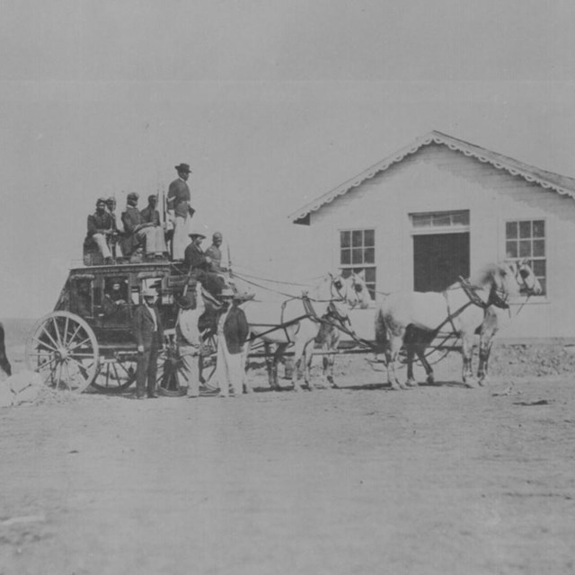 Several soldiers sitting on top of a stagecoach being pulled by a team of horses