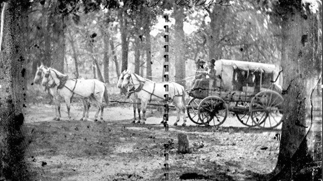 A black and white photo of a stage coach being pulled by horses.