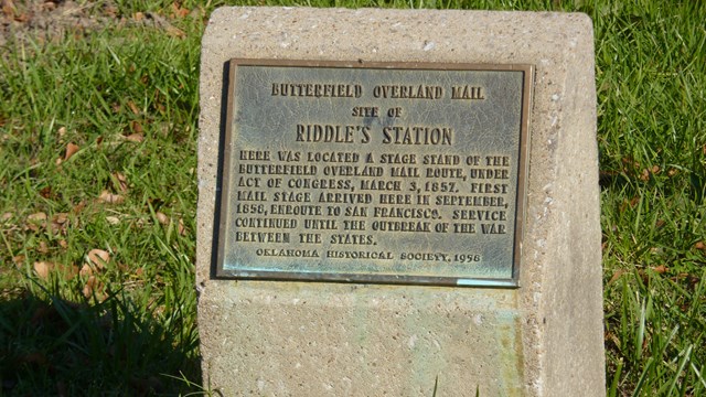 A metal sign on a stone marker in the grass.